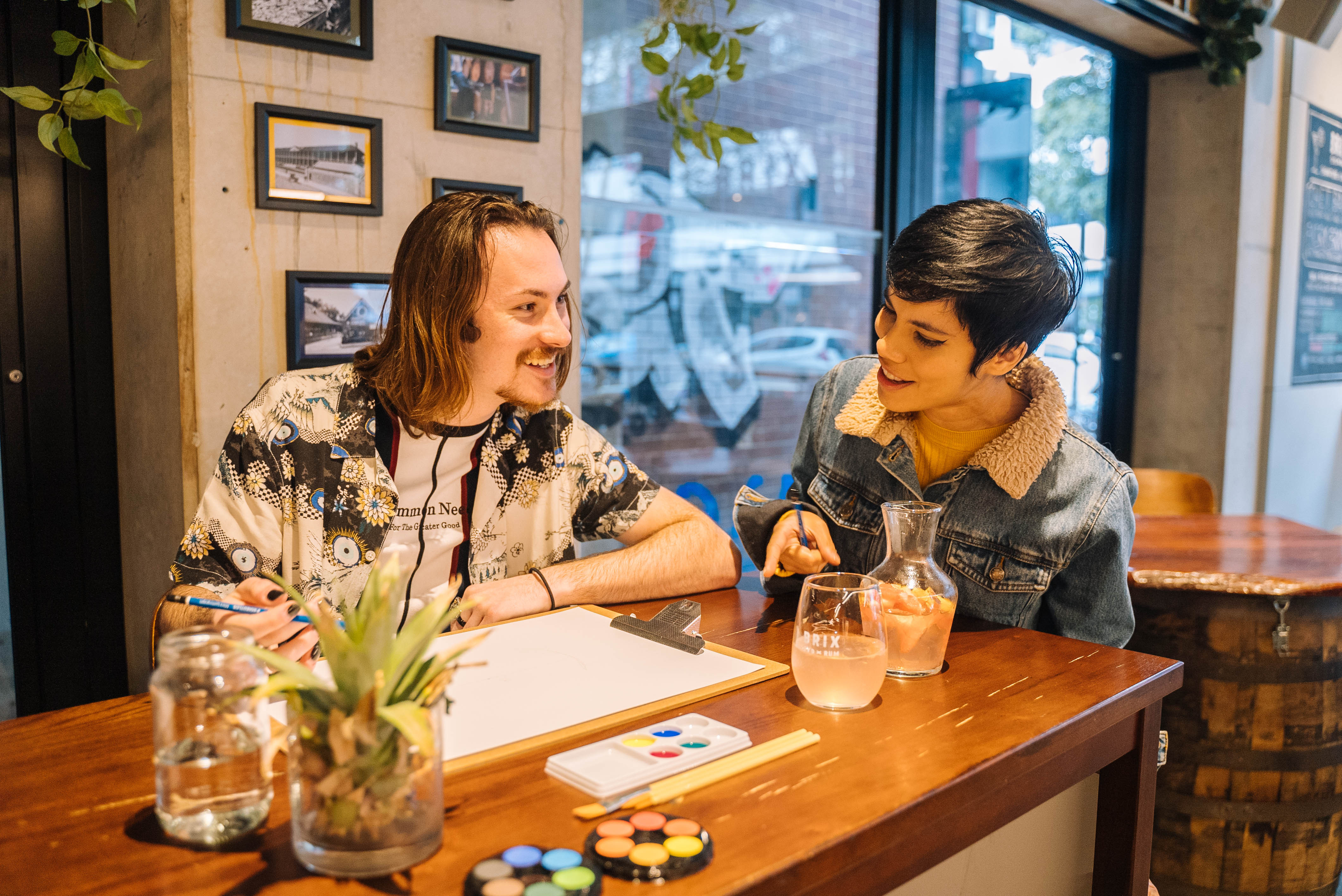 Two people smiling and sharing a drink as they paint a picture together